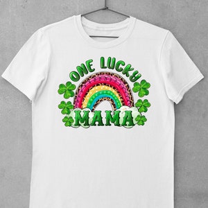 May include: White t-shirt with a rainbow design and the text "One Lucky Mama" in green and black lettering. The rainbow is decorated with leopard print and green shamrocks.