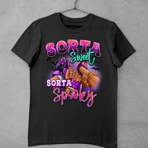 May include: Black t-shirt featuring a graphic design of a pair of feet wearing high heels and the text "Sorta Sweet Sorta Spooky".