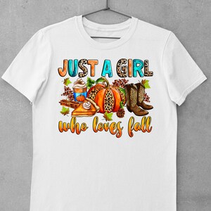 May include: White t-shirt with the text "Just a girl who loves fall" in orange, blue, and brown. The text is surrounded by a pumpkin, boots, a slice of pie, and a cup of coffee.
