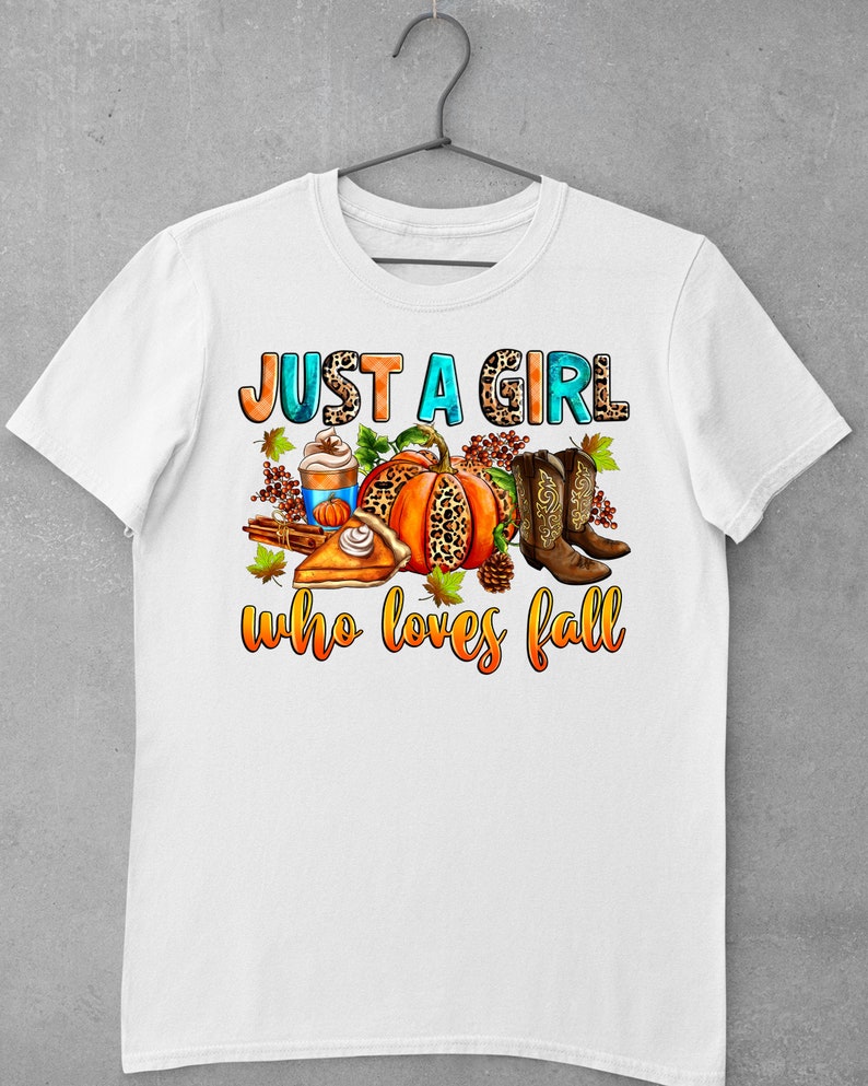 May include: White t-shirt with the text "Just a girl who loves fall" in orange, blue, and brown. The text is surrounded by a pumpkin, boots, a slice of pie, and a cup of coffee.