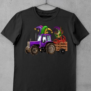 Pu&ograve; includere: Una maglietta nera con un trattore viola che tira un carro con un gambero rosso che indossa un cappello da giullare viola, verde e oro.