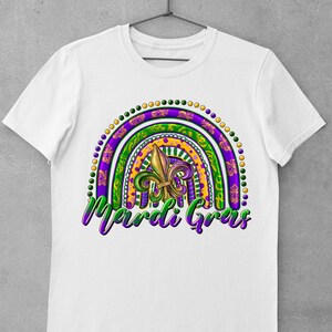 Puede incluir: Camiseta blanca con un dise&ntilde;o de arco&iacute;ris de Mardi Gras colorido con una flor de lis y el texto "Mardi Gras".