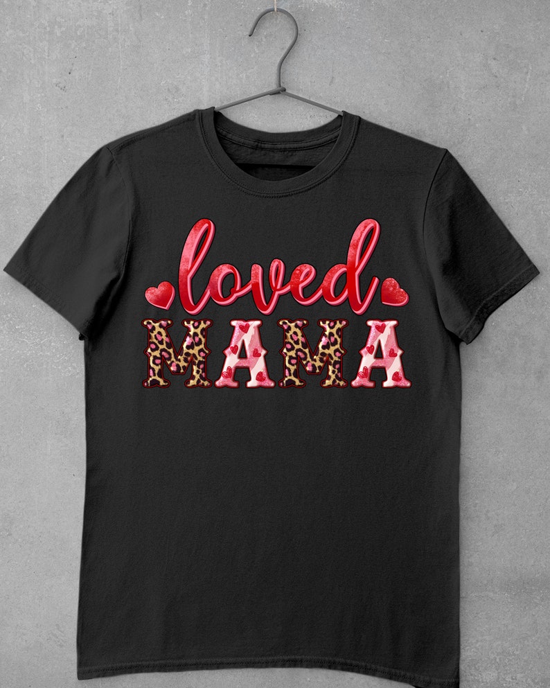 K&ouml;nnte beinhalten: Schwarzes T-Shirt mit dem Text "loved" in Rot mit einem Herz auf jeder Seite und dem Wort "MAMA" in gro&szlig;en Buchstaben mit einem Leopardenmuster und rosa Herzen.