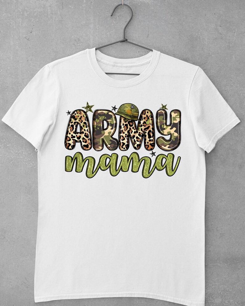 May include: White t-shirt with the text "ARMY mama" in a camouflage and leopard print design. The word "ARMY" features a military helmet graphic. The shirt is hanging on a hanger against a gray background.
