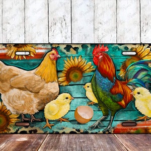 May include: A colorful license plate featuring a rooster, a hen, and three chicks. The background is a turquoise blue with a wooden plank design and sunflowers.