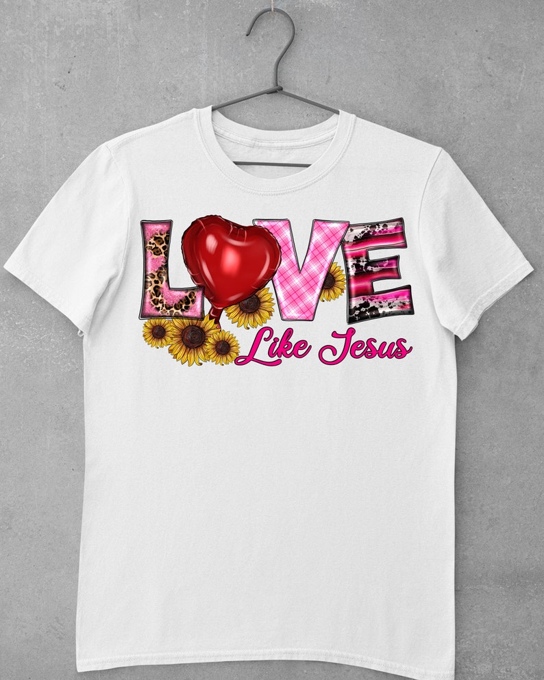 May include: White t-shirt featuring the word "LOVE" in a decorative font with a red heart balloon and sunflowers. The word "LOVE" has a pink leopard print, pink plaid, and black and pink cow print design. The phrase "Like Jesus" is written in pink script.