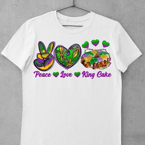 May include: White t-shirt with a peace sign, heart, and king cake graphic. The text "Peace Love King Cake" is printed below the graphic.