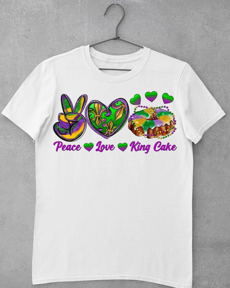 May include: White t-shirt with a peace sign, heart, and king cake graphic. The text "Peace Love King Cake" is printed below the graphic.