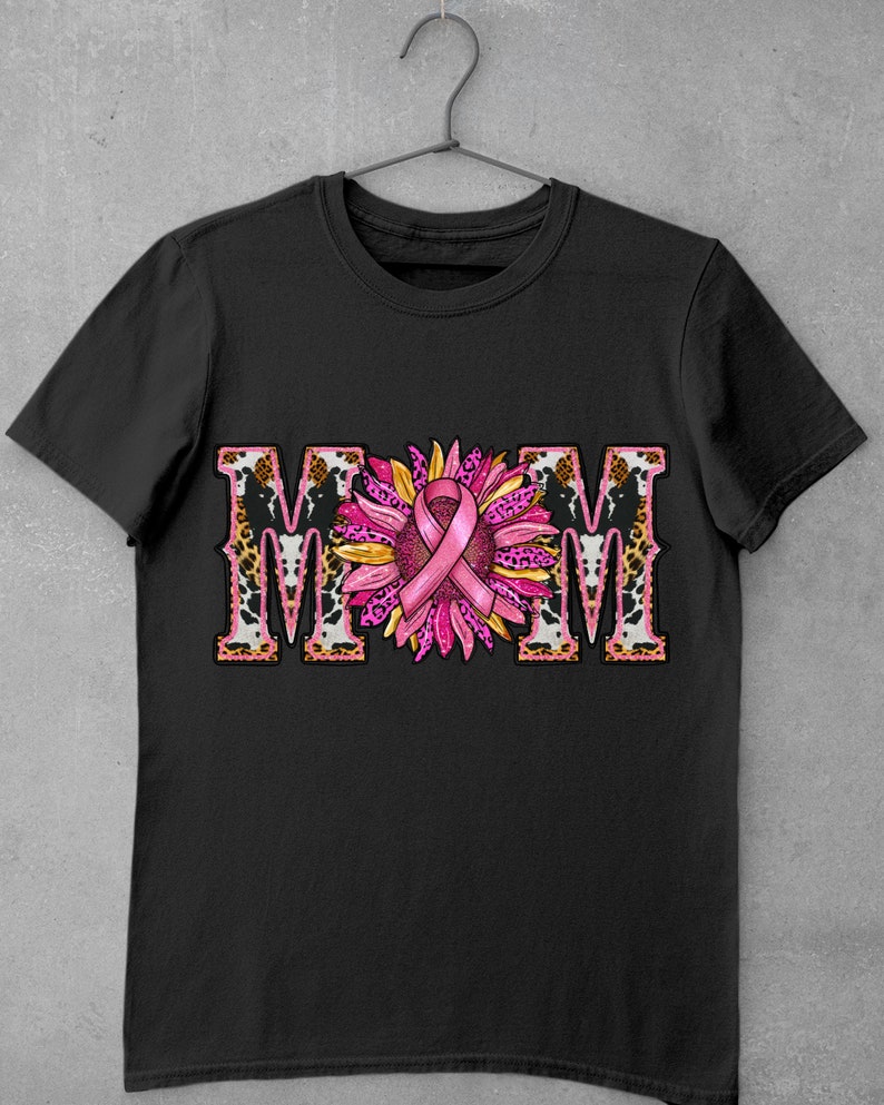 May include: Black t-shirt with a pink ribbon and sunflower design. The word "MOM" is spelled out in large letters with a leopard print background.