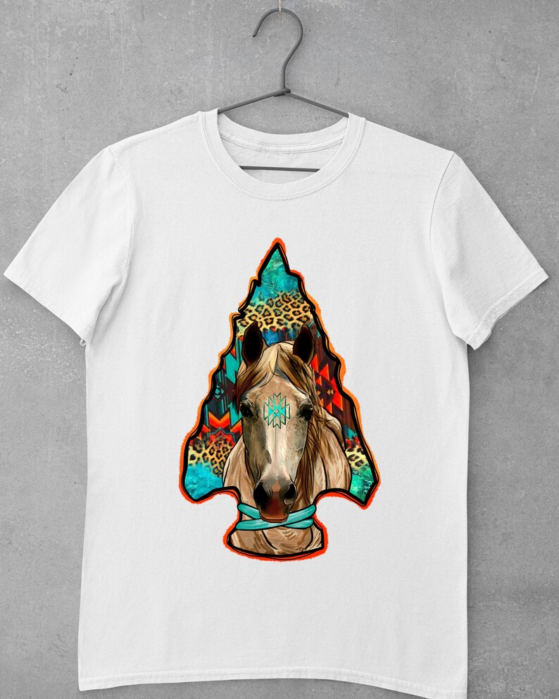 May include: White t-shirt featuring a colourful graphic of a horse's head within an arrowhead design. The arrowhead is filled with geometric patterns and animal print.