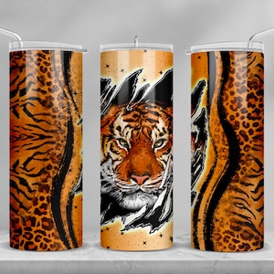 May include: A stainless steel tumbler featuring a tiger face design. The tiger is peeking out from behind a torn, orange and black leopard print background. The tumbler has a lid and a straw.