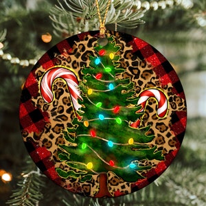 May include: Round Christmas ornament with a red and black plaid background. A green Christmas tree with white lights and candy canes is centered on the ornament. The tree is surrounded by a leopard print pattern.