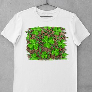 May include: White t-shirt with a green shamrock and leopard print design on a wood background.