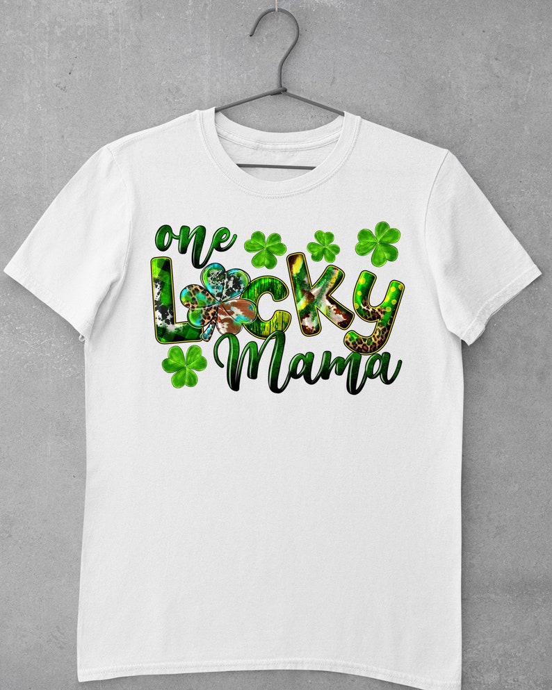 May include: White t-shirt with a green, black, and brown graphic that says "one lucky mama" with four green shamrocks.