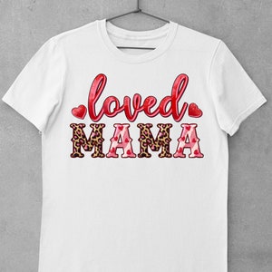 K&ouml;nnte beinhalten: Wei&szlig;es T-Shirt mit dem Text "loved" in Rot mit Herzen auf beiden Seiten und "MAMA" in Rot mit Leopardenmuster und Herzen.