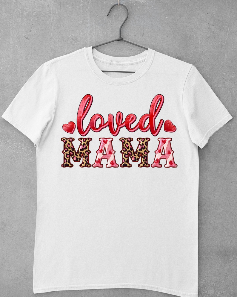 K&ouml;nnte beinhalten: Wei&szlig;es T-Shirt mit dem Text "loved" in Rot mit Herzen auf beiden Seiten und "MAMA" in Rot mit Leopardenmuster und Herzen.