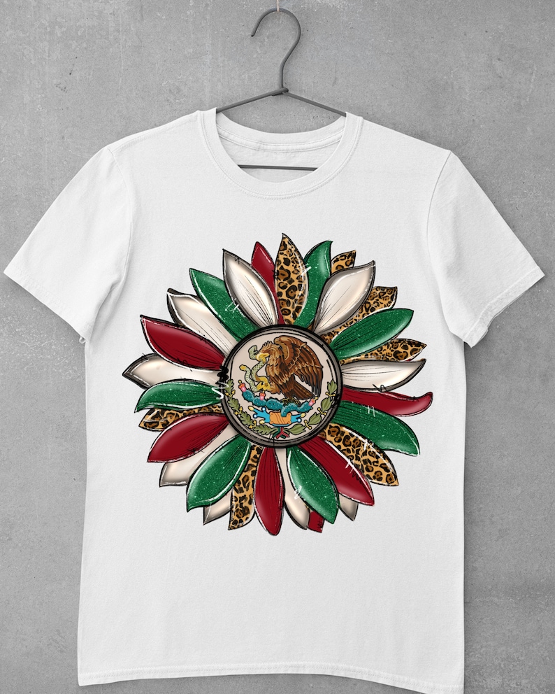May include: White t-shirt with a green, white, and red flower design. The center of the flower features the Mexican coat of arms with an eagle perched on a cactus. The flower petals are accented with a leopard print.
