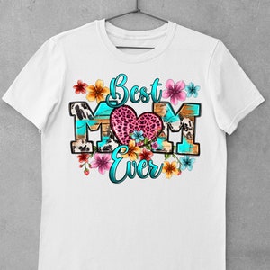 May include: White t-shirt with a graphic design that says "Best Mom Ever" in blue and pink lettering. The graphic features a heart with a leopard print design and colorful flowers.
