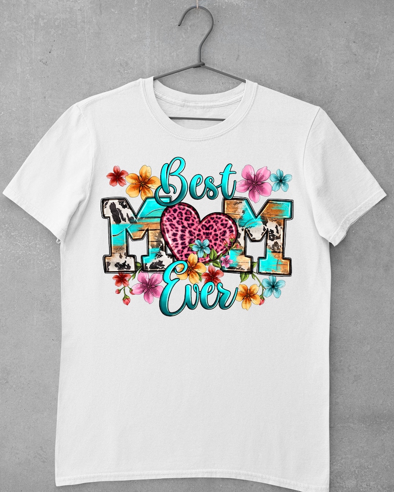 May include: White t-shirt with a graphic design that says "Best Mom Ever" in blue and pink lettering. The graphic features a heart with a leopard print design and colorful flowers.