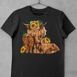 May include: A black t-shirt with a graphic of a Highland cow with two calves. The cow is wearing a sunflower crown. The graphic is in shades of brown, yellow, and green.