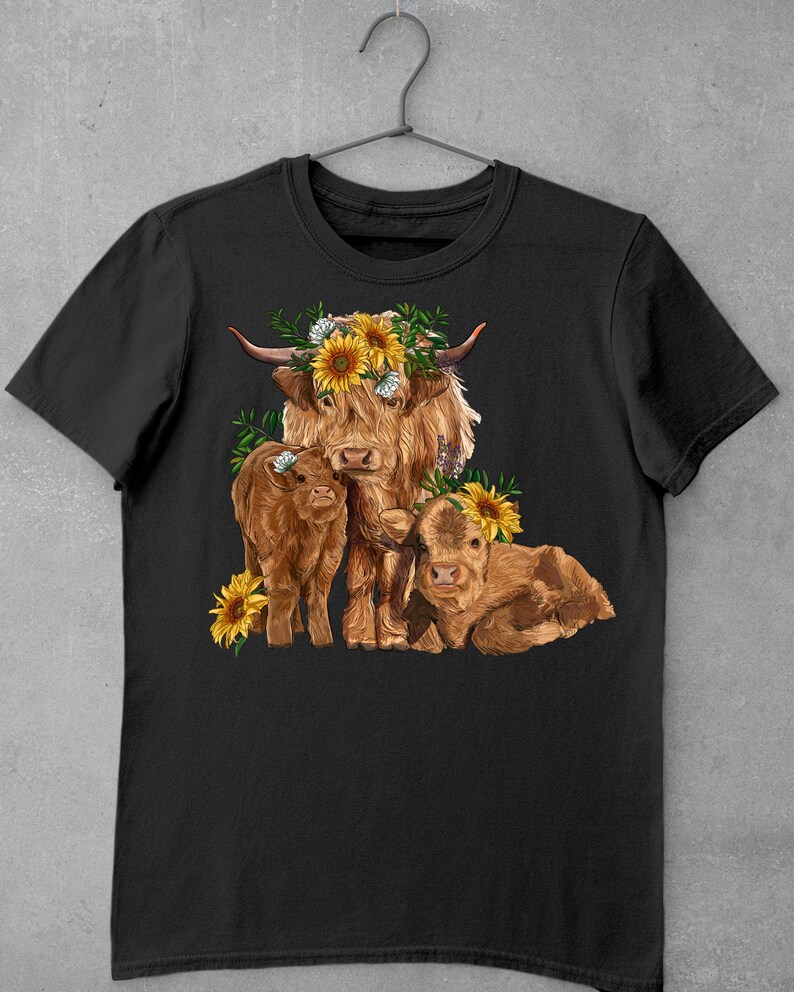 May include: A black t-shirt with a graphic of a Highland cow with two calves. The cow is wearing a sunflower crown. The graphic is in shades of brown, yellow, and green.