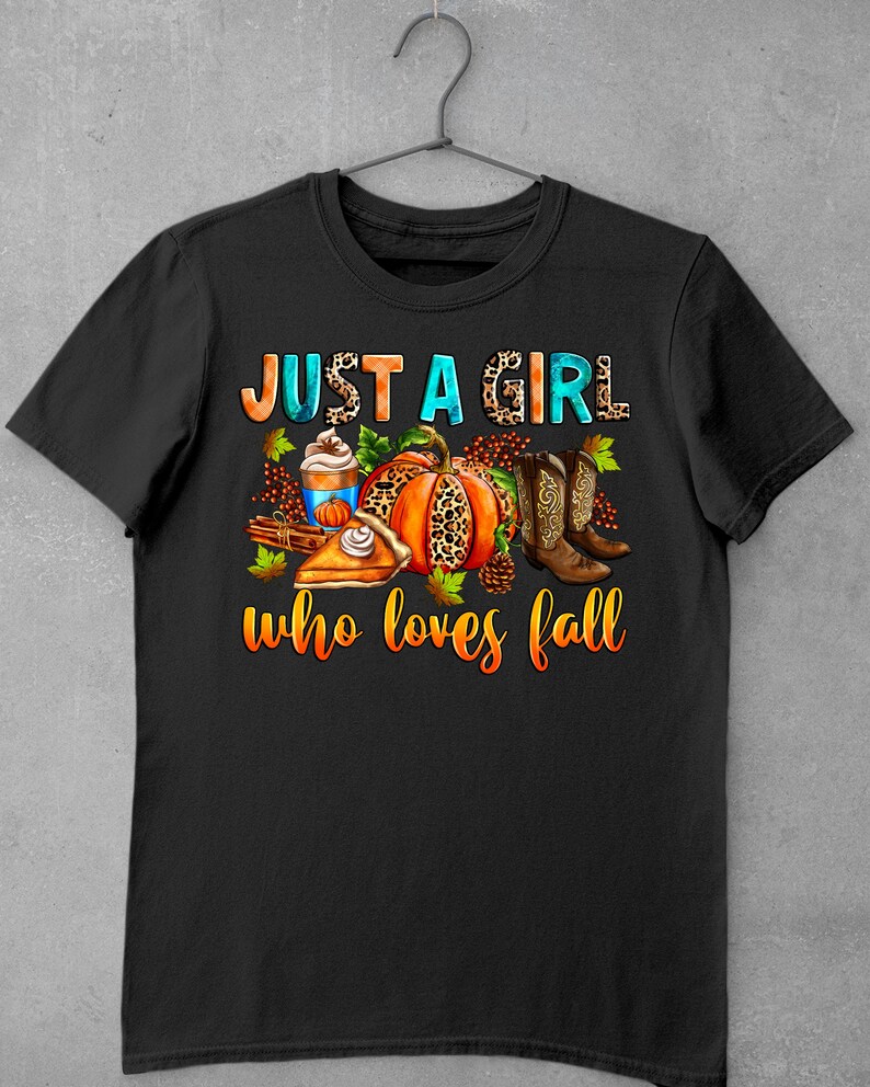 May include: Black t-shirt with the text "Just a girl who loves fall" in white and blue. The text is surrounded by fall-themed imagery, including a pumpkin, pie, boots, and a cup of coffee.