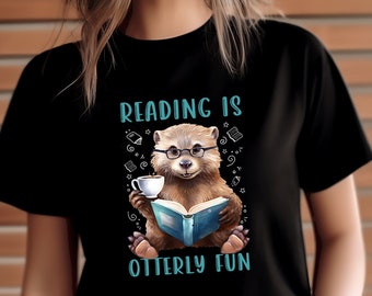 May include: Black t-shirt with a cartoon otter wearing glasses and reading a book. The text "Reading is otter-ly fun" is printed on the shirt.
