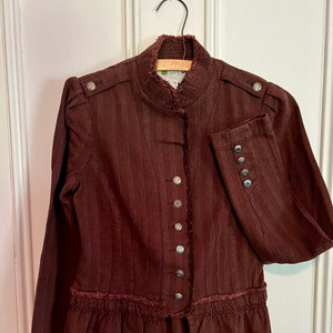 May include: A brown striped jacket with a ruffled hem and a stand-up collar. The jacket has a button closure and silver buttons.