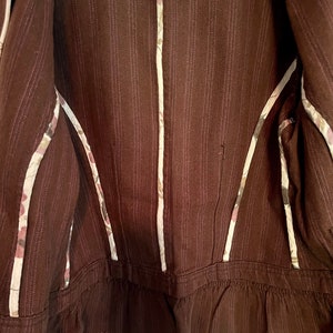 May include: Brown striped jacket with a white floral trim. The jacket has a ruffled hem and a zipper closure.
