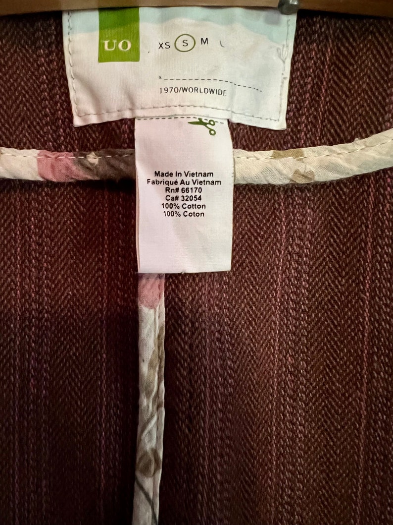 May include: A brown cotton jacket with a white floral print lining. The tag reads "UO" and "Made in Vietnam" with the RN and CA numbers. The size tag shows XS, S, M, and L.