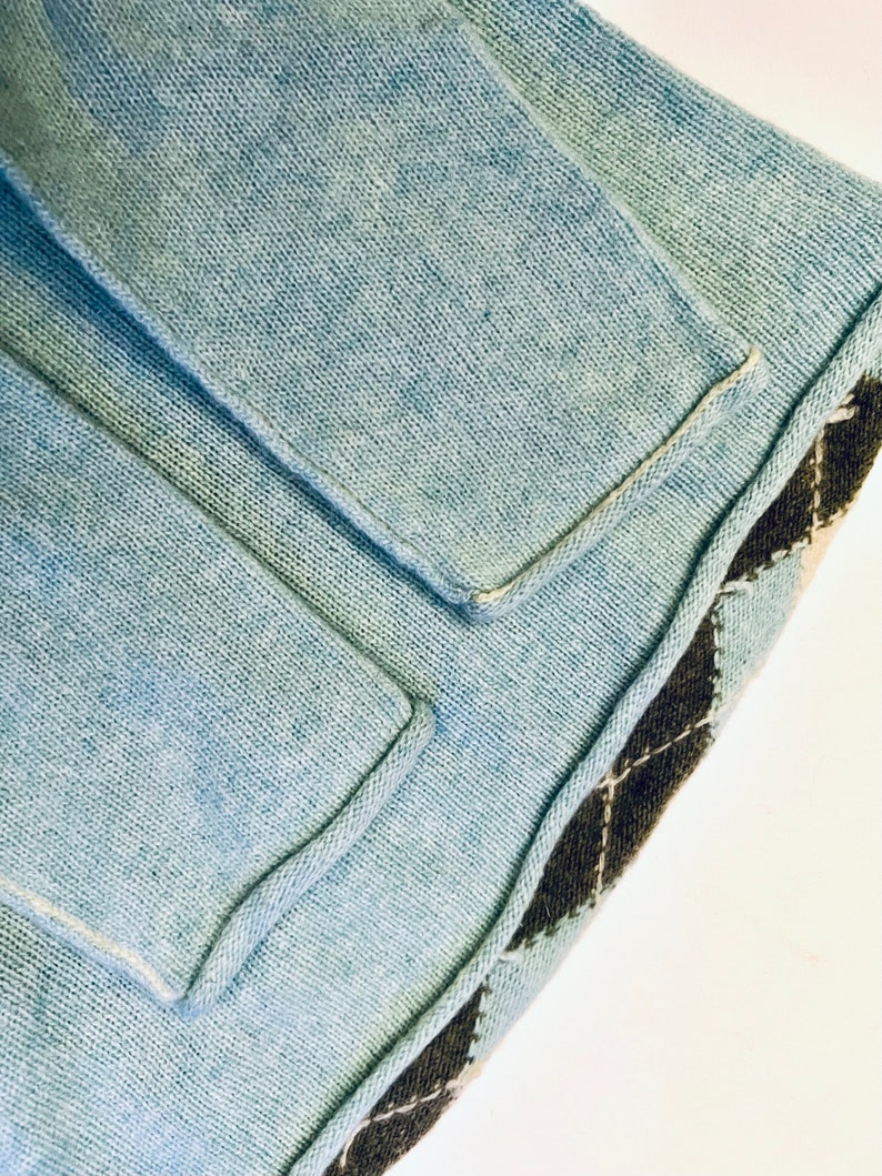 Puede incluir: Un su&eacute;ter de punto azul claro con un ribete de patr&oacute;n de diamante marr&oacute;n y blanco. El su&eacute;ter tiene un bolsillo en la parte delantera.