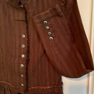 May include: A brown striped jacket with a ruffled hem and silver buttons. The jacket has a mandarin collar and long sleeves.