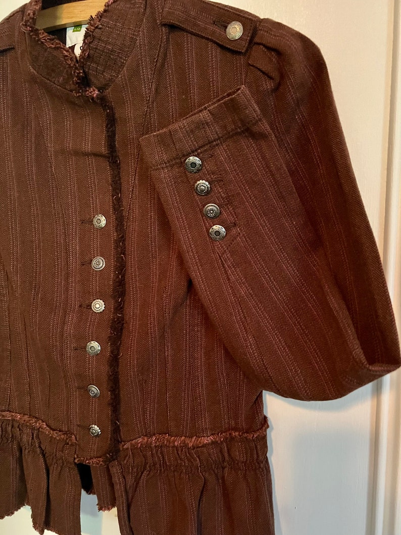 May include: A brown striped jacket with a ruffled hem and silver buttons. The jacket has a mandarin collar and long sleeves.