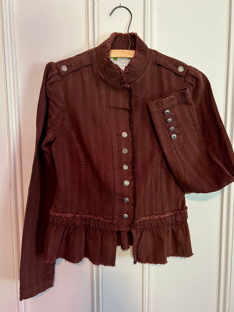 May include: A brown striped jacket with a ruffled hem and a stand-up collar. The jacket has a button closure and silver buttons.