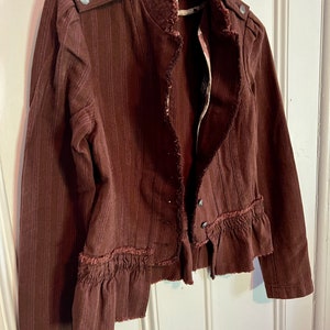 May include: A brown striped jacket with a ruffled hem and frayed edges. The jacket has a stand-up collar and a button closure.