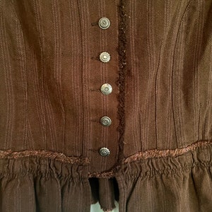 May include: A brown, striped, ruffled jacket with a row of silver buttons down the front.