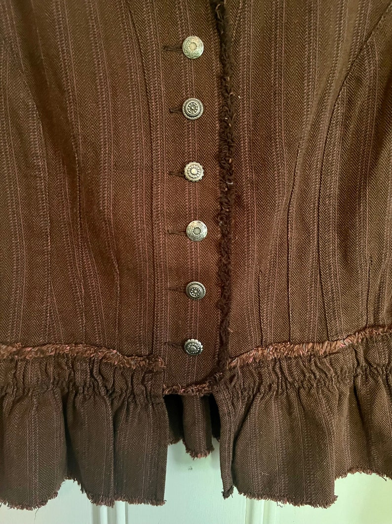 May include: A brown, striped, ruffled jacket with a row of silver buttons down the front.