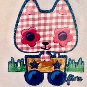 May include: A pink and white gingham cat with blue glitter trim and large pink flowers with blue centres for eyes. The cat is pulling a wooden wagon with blue wheels and stars. The wagon is on a white background with green grass.