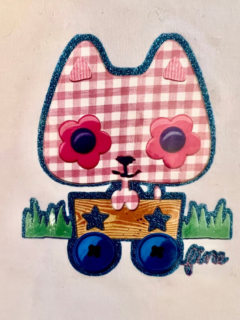 May include: A pink and white gingham cat with blue glitter trim and large pink flowers with blue centres for eyes. The cat is pulling a wooden wagon with blue wheels and stars. The wagon is on a white background with green grass.