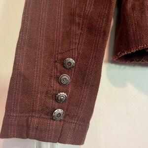 May include: A brown striped jacket with silver buttons on the cuff. The jacket has a herringbone pattern.