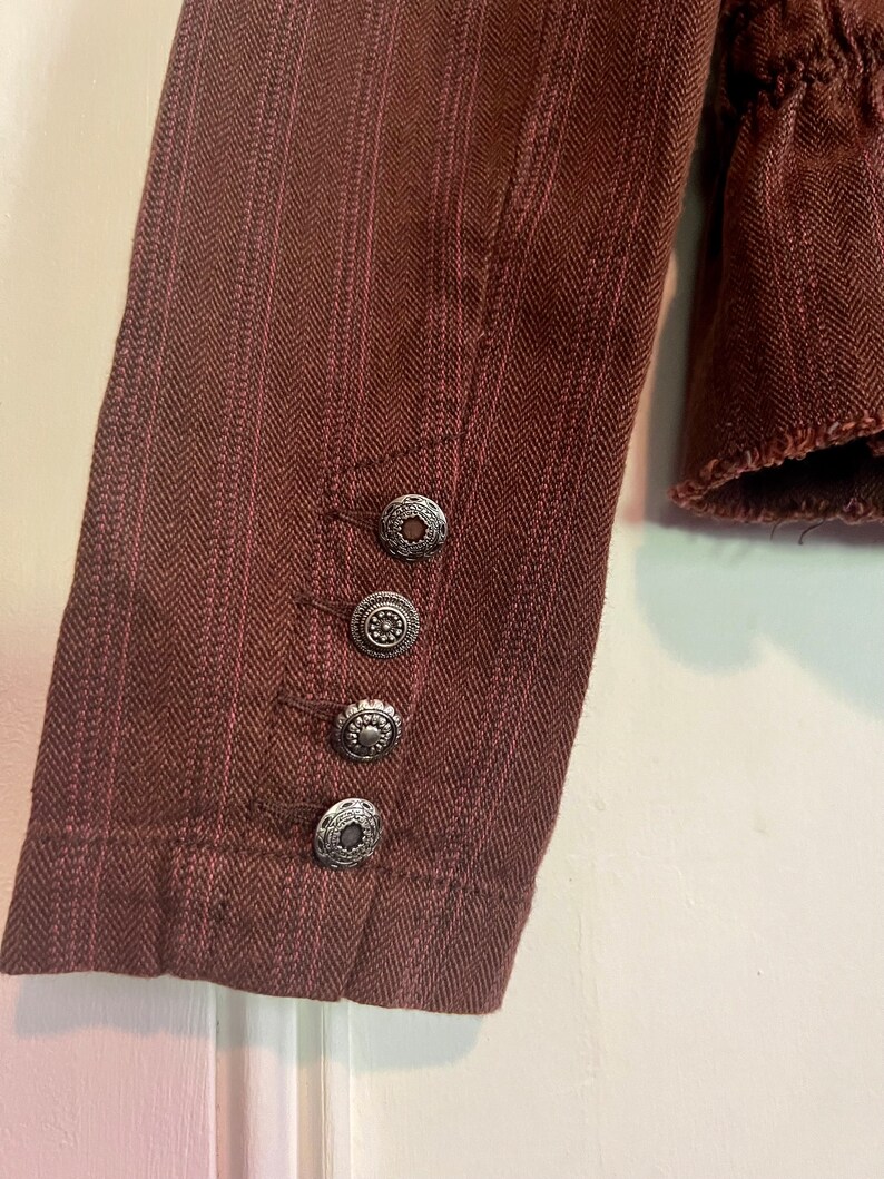 May include: A brown striped jacket with silver buttons on the cuff. The jacket has a herringbone pattern.