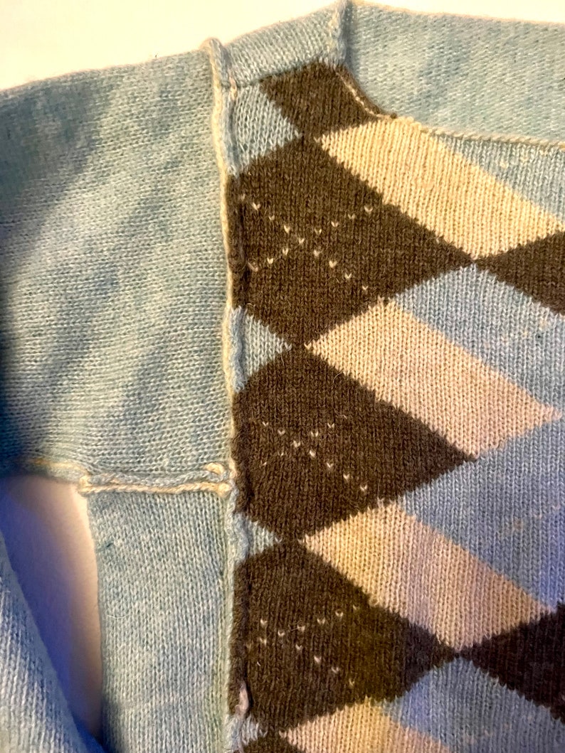 Puede incluir: Primer plano de un su&eacute;ter azul con un patr&oacute;n de rombos marr&oacute;n, blanco y azul. El su&eacute;ter est&aacute; tejido y tiene una costura en el lateral.