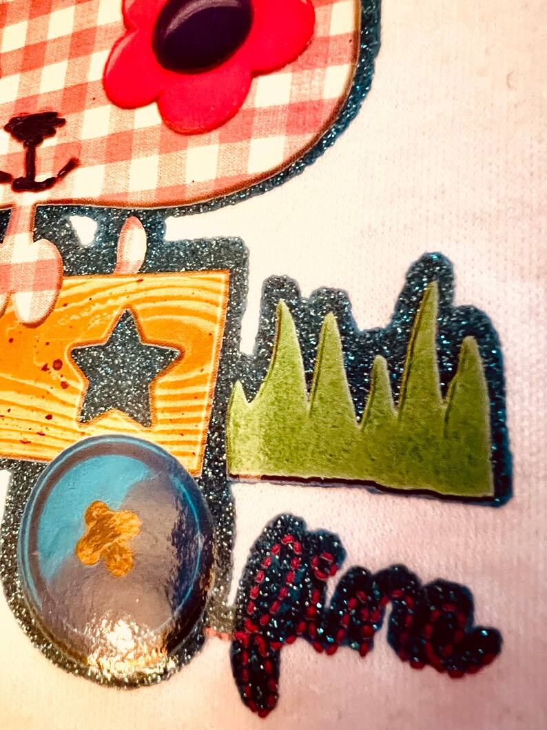 May include: A white fabric patch with a pink and white gingham design, a red flower with a black centre, a blue star, a yellow and brown wooden box, green grass, a blue and gold ball, and a red and blue sparkly word "fun".