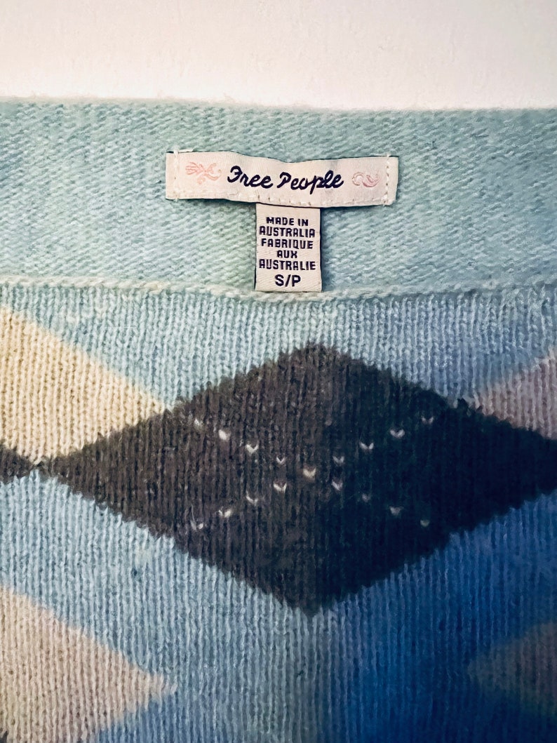 Puede incluir: Un su&eacute;ter azul y blanco con un patr&oacute;n de diamantes. El su&eacute;ter tiene una etiqueta de Free People que dice "Made in Australia, Fabrique aux Australie, S/P".