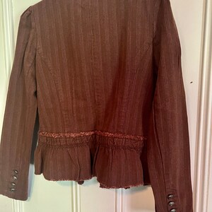 May include: A brown striped blazer with a ruffled hem and frayed edges. The blazer has a high collar and long sleeves with button cuffs.
