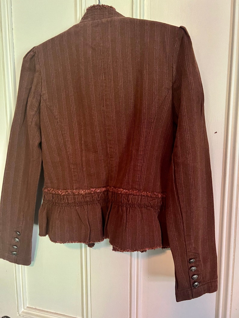 May include: A brown striped blazer with a ruffled hem and frayed edges. The blazer has a high collar and long sleeves with button cuffs.