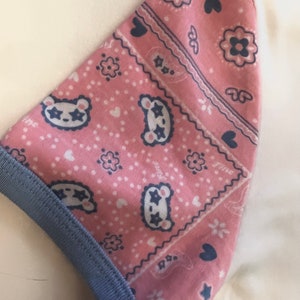 May include: Pink fabric with a blue and white bandana print featuring stars, hearts, and small animal faces. The fabric has a blue trim.