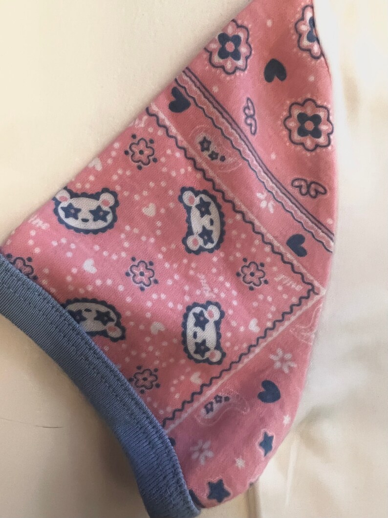 May include: Pink fabric with a blue and white bandana print featuring stars, hearts, and small animal faces. The fabric has a blue trim.