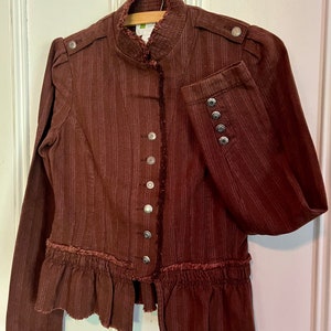 May include: A brown striped jacket with a ruffled hem and silver buttons. The jacket has a mandarin collar and long sleeves.