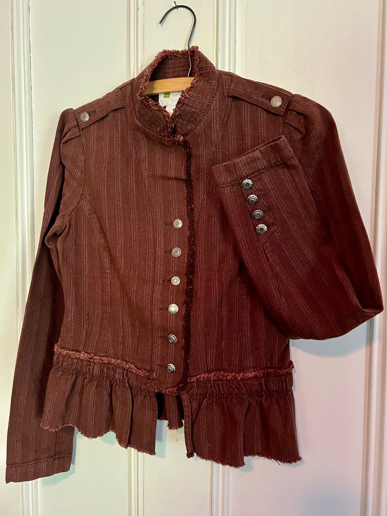 May include: A brown striped jacket with a ruffled hem and silver buttons. The jacket has a mandarin collar and long sleeves.